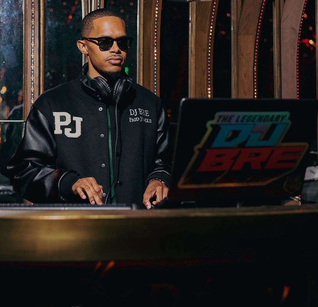 DJ BRE, founder of Paid Jungle, wearing his personal Paid Jungle jacket at the DJ booth